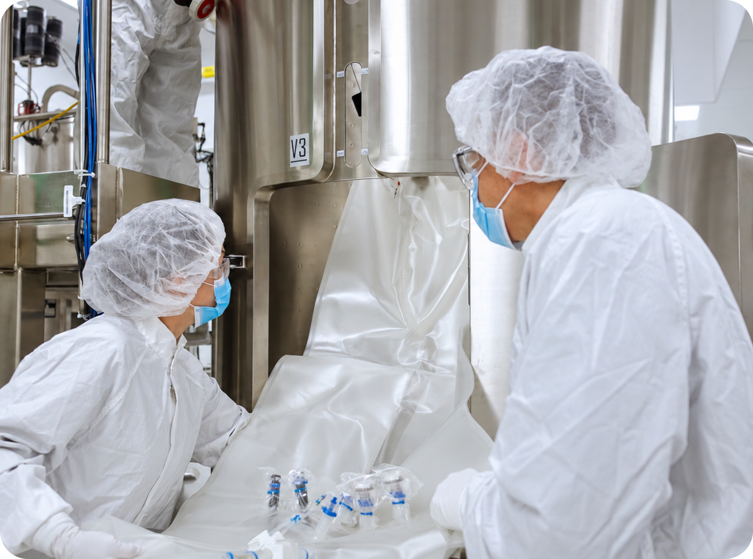 Two cleanroom technicians working beside a stainless-steel processing vessel